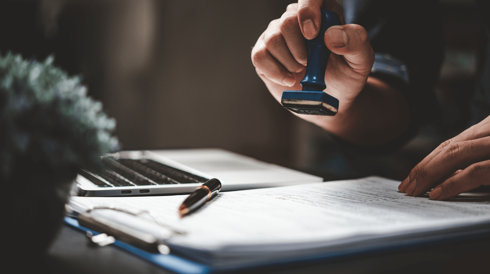 Person stamping paperwork on a clipboard next to a laptop — due diligence review